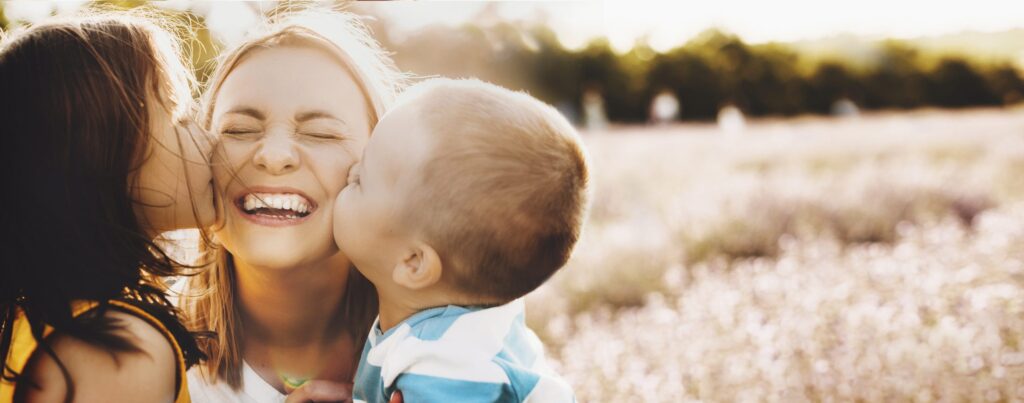 Mother laughing as her two children kiss her cheeks
